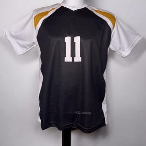 May include: Black and white athletic jersey with gold accents on the shoulders. The number "11" is prominently displayed in white on the front. The jersey has a V-neck and short sleeves. The text "KQ Jersey" is printed at the bottom.