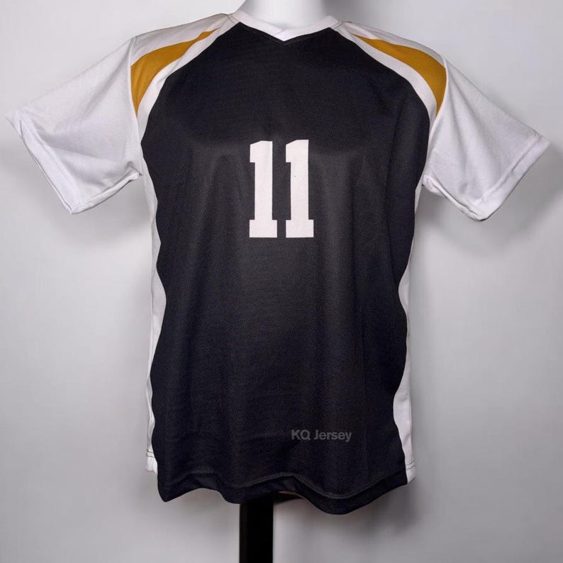 May include: Black and white athletic jersey with gold accents on the shoulders. The number "11" is prominently displayed in white on the front. The jersey has a V-neck and short sleeves. The text "KQ Jersey" is printed at the bottom.