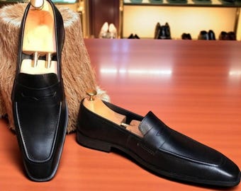 Könnte beinhalten: Ein Paar schwarze Leder-Loafer mit Schuhspannern aus Holz. Die Schuhe haben ein klassisches Design mit runder Spitze und niedrigem Absatz. Im Hintergrund sind weitere Schuhe zu sehen.