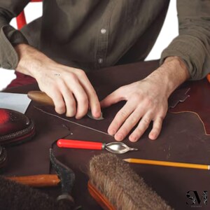 May include: A shoemaker's workshop with tools and materials. The image shows a person working on leather, using a knife and other tools. A partially finished shoe is visible, along with brushes, pencils, and other crafting supplies.