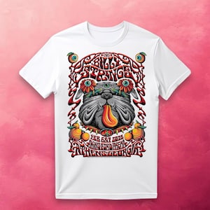 May include: White t-shirt featuring a psychedelic bulldog design with the text "String Cheese Incident" and event details. The graphic includes vibrant colors, flowers, and a peace symbol, creating a retro concert poster aesthetic.