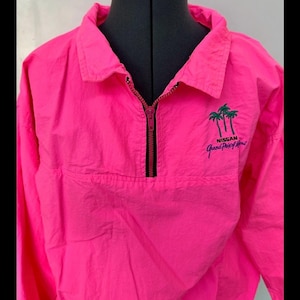 May include: Bright pink pullover jacket with a half-zip closure and a collared neckline. The jacket features a small embroidered design of palm trees and the text "NISSAN Grand Prix of Miami" in green and white.