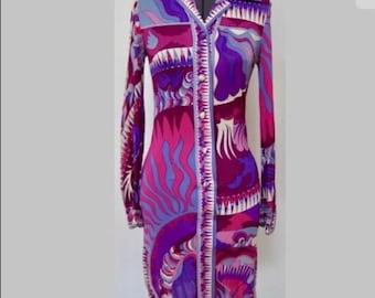 Pode incluir: Vestido de manga comprida com botões, com uma estampa psicodélica vibrante em tons de roxo, rosa e azul. O vestido apresenta um colarinho e uma silhueta ajustada, mostrando um design artístico e arrojado. O vestido é exibido em um manequim.