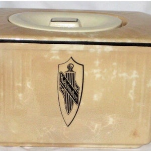 May include: A beige ceramic teapot with a black trim and a lid. The teapot has a handle and a spout. The front of the teapot has a black and white logo that says "Kelvinator".