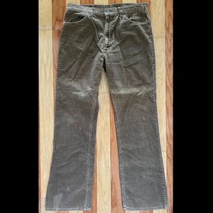 May include: A pair of brown corduroy pants. The pants have a classic five-pocket design with a button and zipper closure. The corduroy fabric has a ribbed texture and a slight sheen. The pants are in good condition and appear to be well-worn.