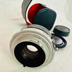 May include: A silver camera lens with a black interior, a black leather case with a red lining, and two black lens caps. The lens has the text "CONVERTER 2X" on it.
