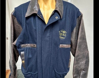 May include: A navy blue and brown varsity jacket with leather sleeves. The jacket has a zipper closure and a gold embroidered logo that says "The China Clipper".