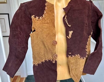 May include: A two-tone suede jacket in shades of brown and tan, with decorative stitching and button closures. The jacket is displayed on a mannequin, showcasing its unique patchwork design and vintage aesthetic.
