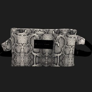 Op de afbeelding: Een zwart-wit heuptasje met slangenpatroon, met een zwarte verstelbare riem en gesp. De tas heeft een rechthoekige vorm met een klein zwart label in het midden.