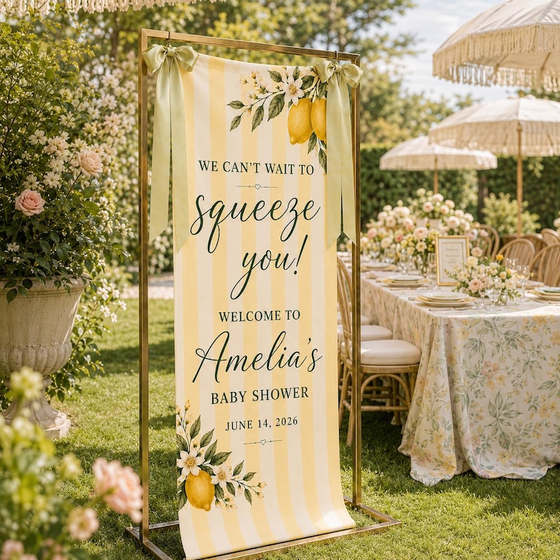 Puede incluir: Un cartel rectangular vertical con rayas amarillas y blancas, decorado con ilustraciones de limones y flores blancas. El texto dice: WE CAN'T WAIT TO squeeze you! WELCOME TO Amelia's BABY SHOWER JUNE 14, 2026. Est&aacute; sujeto a un marco de metal dorado.