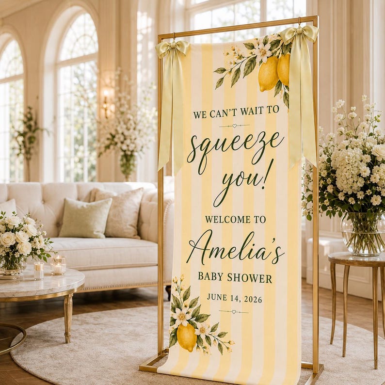 Puede incluir: Un cartel vertical con rayas amarillas y blancas, decorado con ilustraciones de limones y flores. El texto dice: WE CAN'T WAIT TO squeeze you! WELCOME TO Amelia's BABY SHOWER JUNE 14, 2026. El cartel est&aacute; sujeto por un marco de color dorado.