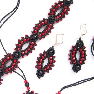May include: A handmade jewelry set featuring a necklace, bracelet, and earrings. The pieces are black with red beads and black accent beads. The earrings have silver hooks. The jewelry is displayed on a white background.