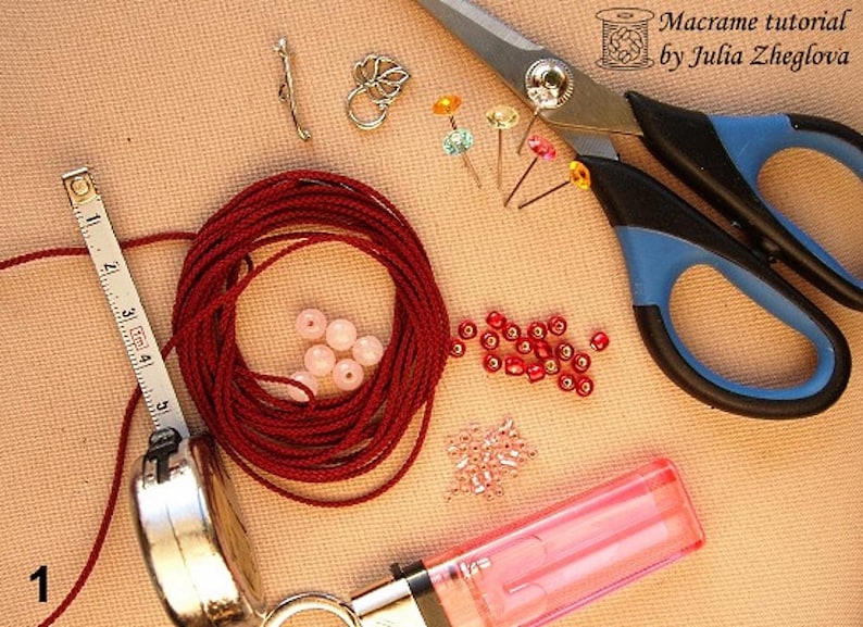 May include: A collection of macrame supplies, including red cord, pink beads, and various metal findings. A tape measure shows inches. Scissors with blue handles and the text "Macrame tutorial by Julia Zheglova" are also visible, suggesting a crafting project.