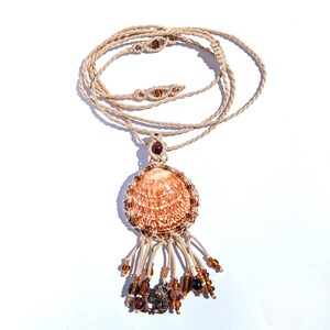 Puede incluir: Collar de macram&eacute; hecho a mano con un colgante de concha. El colgante es una concha grande y estampada, rodeada de cuentas marrones. Cuelga de un cord&oacute;n beige. Cuentas marrones y un peque&ntilde;o dije cuelgan debajo.