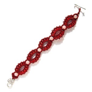 May include: A handmade macrame bracelet in a deep red color, featuring an intricate woven design. The bracelet is adorned with small, clear beads and light pink gemstone accents. It has a silver-tone clasp and is displayed on a white background.