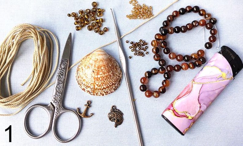 Puede incluir: Una colecci&oacute;n de materiales de artesan&iacute;a que incluye una concha, tijeras, cuentas, un ganchillo, una pulsera y un estuche decorativo. Los art&iacute;culos est&aacute;n dispuestos sobre una superficie azul claro, lo que sugiere un tema de artesan&iacute;a o fabricaci&oacute;n de joyas.