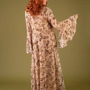 Puede incluir: Un vestido maxi largo y fluido con estampado floral en tonos marrones y beige. El vestido tiene un escote en V y mangas largas con pu&ntilde;os acampanados.