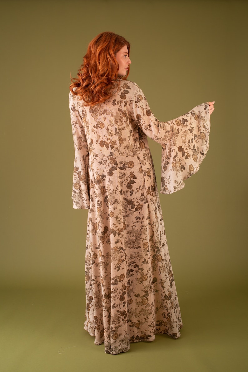 Puede incluir: Un vestido maxi largo y fluido con estampado floral en tonos marrones y beige. El vestido tiene un escote en V y mangas largas con pu&ntilde;os acampanados.