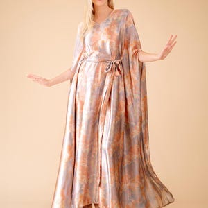 May include: A long, flowing, pink and purple tie-dye maxi dress with a V-neck and a sash tie at the waist.