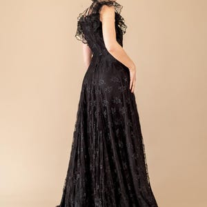 Pode incluir: Um vestido longo de renda preta com decote com babados e mangas curtas. O vestido apresenta um corpete justo e uma saia fluida, criando uma silhueta elegante. Os intrincados detalhes de renda adicionam textura ao traje formal.