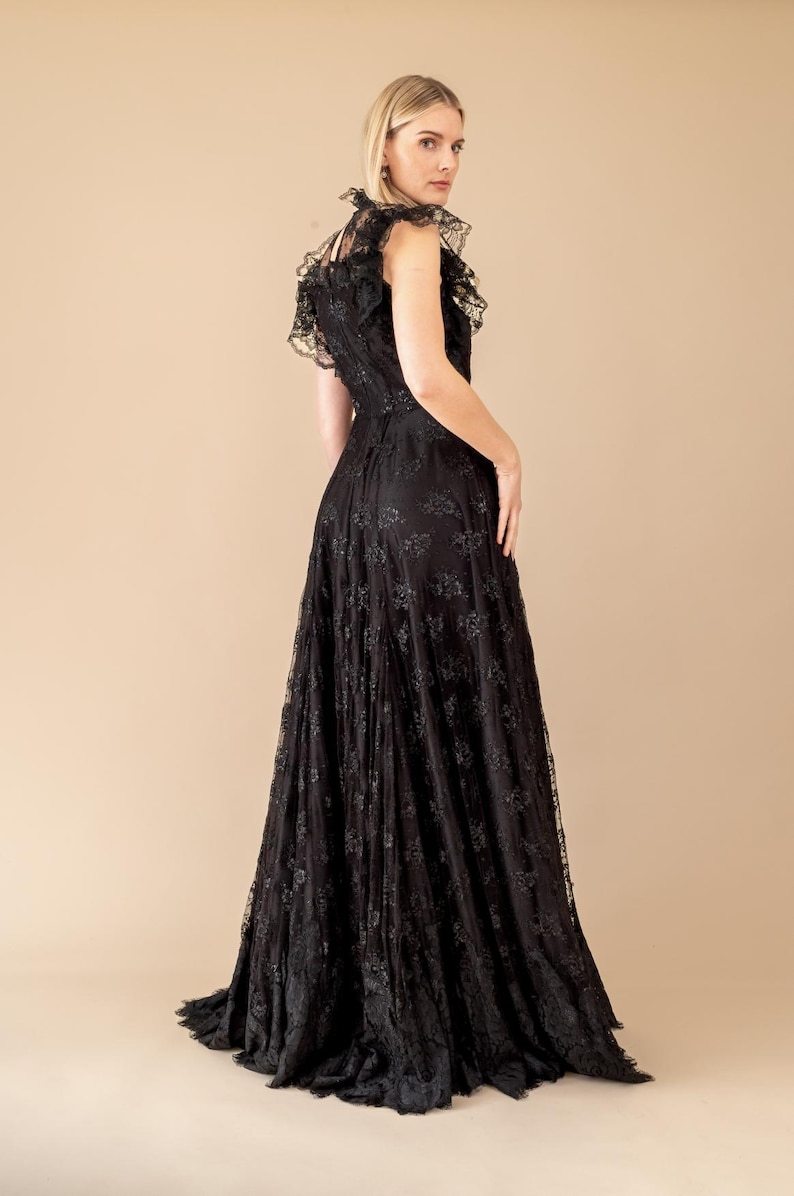 Pode incluir: Um vestido longo de renda preta com decote com babados e mangas curtas. O vestido apresenta um corpete justo e uma saia fluida, criando uma silhueta elegante. Os intrincados detalhes de renda adicionam textura ao traje formal.