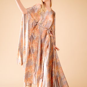 May include: A long, flowing, peach-colored dress with a tie waist and a floral print. The dress is made of a silky material and has a relaxed fit.