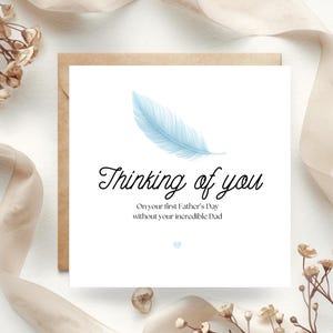 Op de afbeelding: Een witte wenskaart met de tekst "Thinking of you" en een blauwe veertekening. De kaart ligt op een wit oppervlak met een bruine envelop, beige lint en gedroogde bloemen.