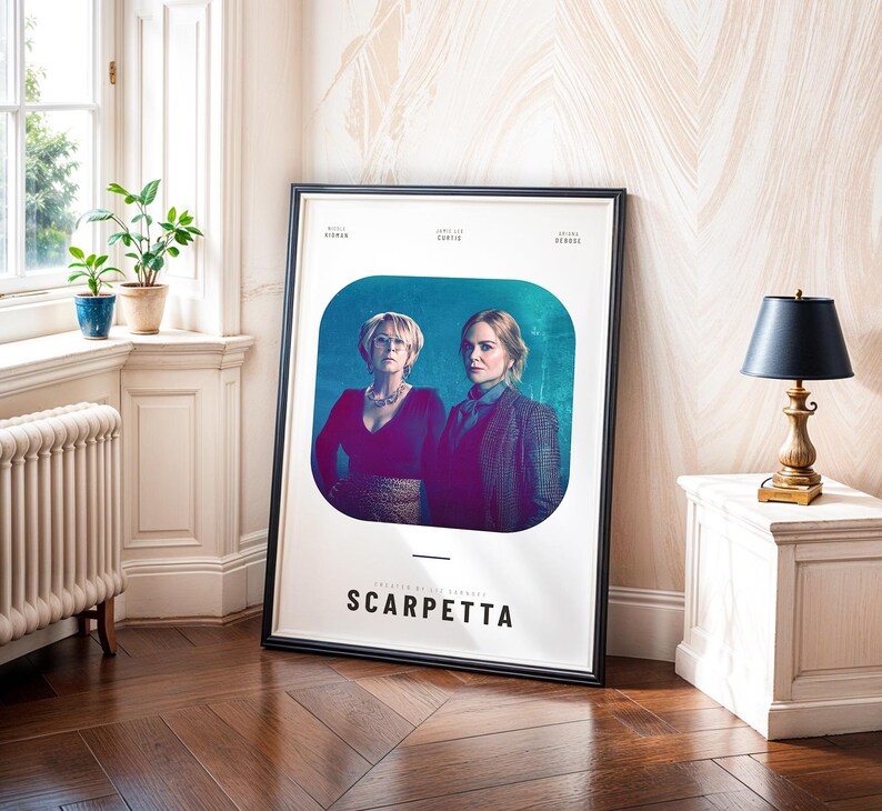 May include: A framed poster featuring two women against a teal background. The poster has the title "SCARPETTA" in large, bold letters. The poster is leaning against a wall in a room with a window and a small table with a lamp.