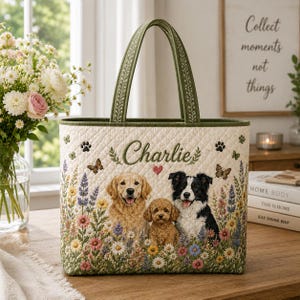 Op de afbeelding: Een gewatteerde draagtas met een crèmekleurige achtergrond, een kleurrijke bloemenprint en drie honden. De naam Charlie is in het groen boven de honden geborduurd, vergezeld van een klein rood hartje, vlinders en pootafdrukken. Heeft groene hengsels.