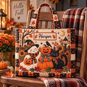 Op de afbeelding: Een gewatteerde tas met de naam Harper, een geest met een heksenhoed, een stapel pompoenen, een zwarte kat en een lantaarn. Het ontwerp bevat herfstbladeren, zonnebloemen en een zwart-oranje ruitpatroon op een crèmekleurige achtergrond.