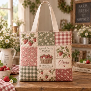 May include: A quilted tote bag featuring a patchwork design of strawberries, floral patterns, and gingham checks in red, green, and cream. The centre panel displays the text Sweet Berry Market, Fresh Fruit Happier Days, and the name Olivia.