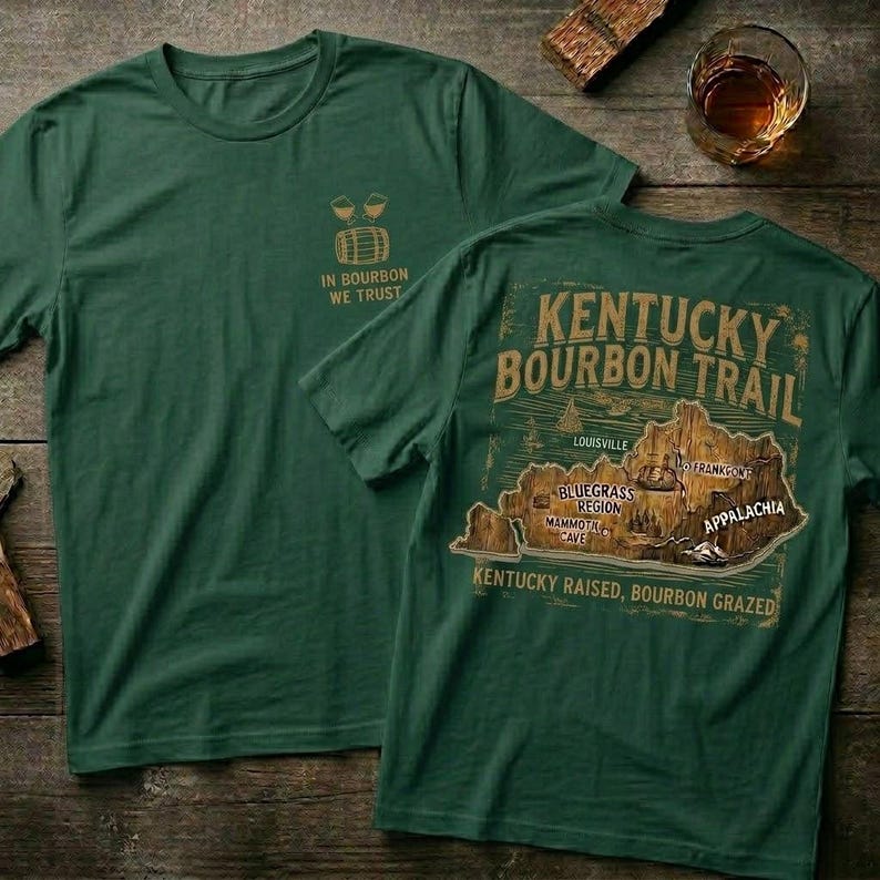 Puede incluir: Dos camisetas verde bosque. Una camiseta tiene un peque&ntilde;o gr&aacute;fico y el texto "IN BOURBON WE TRUST". La otra camiseta presenta un mapa de Kentucky con "KENTUCKY BOURBON TRAIL" y "KENTUCKY RAISED, BOURBON GRAZED".