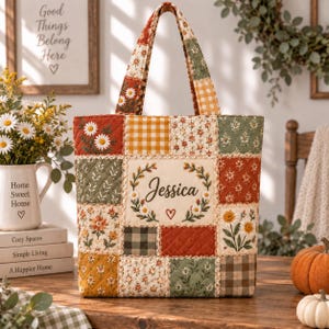 Può includere: Una borsa tote trapuntata con un design patchwork di quadrati di tessuto floreali, a quadretti e tinta unita nei colori autunnali. Il pannello centrale mostra il nome Jessica in corsivo, circondato da una ghirlanda floreale e un cuore.