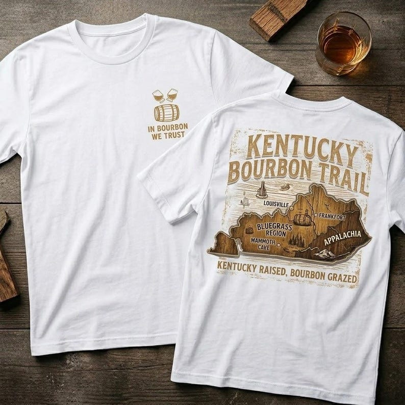 Puede incluir: Camisetas blancas con tem&aacute;tica de bourbon. Una camiseta presenta el texto "IN BOURBON WE TRUST" y un gr&aacute;fico de barril y vasos. La otra camiseta muestra un mapa del Kentucky Bourbon Trail con el texto "KENTUCKY BOURBON TRAIL".