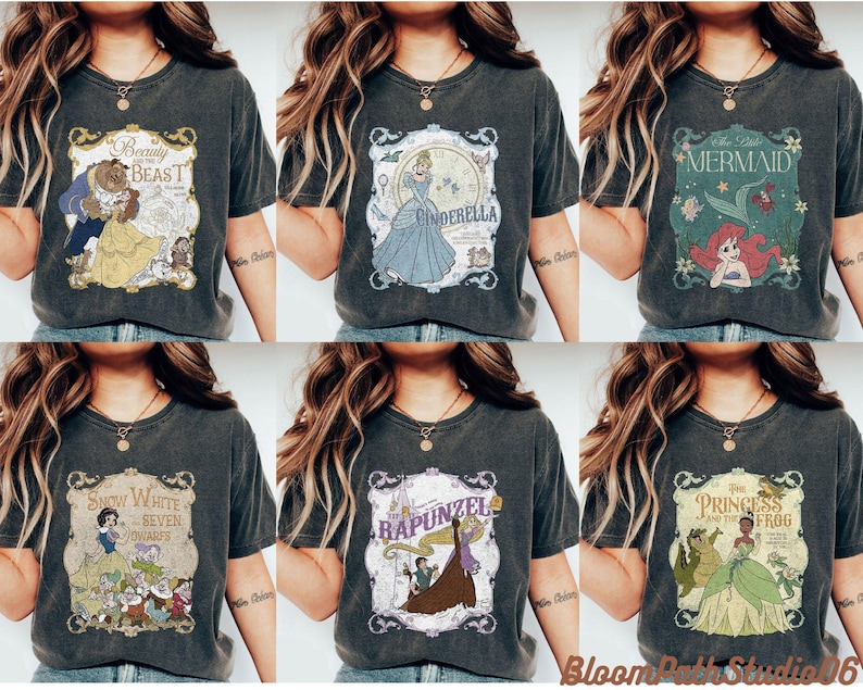 Op de afbeelding: Een collectie van zes antracietgrijze T-shirts met korte mouwen, elk voorzien van een andere vintage-stijl grafische print van een sprookjesfiguur, waaronder Belle en het Beest, Assepoester, De Kleine Zeemeermin, Sneeuwwitje, Rapunzel en Tiana.