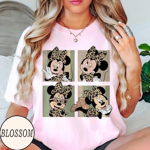K&ouml;nnte beinhalten: Hellrosa T-Shirt mit einem Vier-Panel-Design von Minnie Mouse in verschiedenen Posen, alle mit Leopardenmuster-Schleifen und Outfits. Auf dem T-Shirt steht das Wort "BLOSSOM".