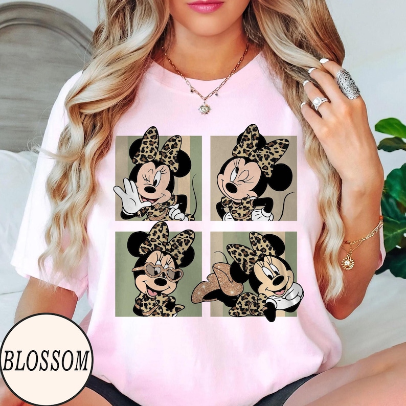 K&ouml;nnte beinhalten: Hellrosa T-Shirt mit einem Vier-Panel-Design von Minnie Mouse in verschiedenen Posen, alle mit Leopardenmuster-Schleifen und Outfits. Auf dem T-Shirt steht das Wort "BLOSSOM".