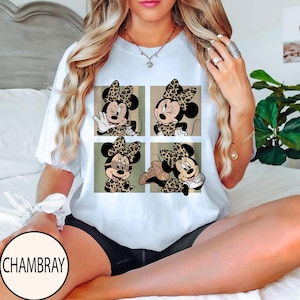 K&ouml;nnte beinhalten: Wei&szlig;es T-Shirt mit einem Vier-Panel-Design von Minnie Mouse in verschiedenen Posen, alle mit Leopardenmuster-Schleifen und -Outfits. Das Shirt hat einen Rundhalsausschnitt und kurze &Auml;rmel. Der Markenname "CHAMBRAY" ist unten links aufgedruckt.