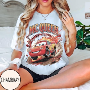 Puede incluir: Una camiseta blanca de manga corta con un gr&aacute;fico del coche de carreras rojo Lightning McQueen y el texto MC QUEEN encima. El dise&ntilde;o incluye llamas, herramientas mec&aacute;nicas y el n&uacute;mero 95 en el lateral del veh&iacute;culo.