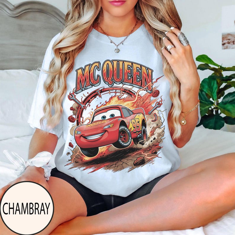 Puede incluir: Una camiseta blanca de manga corta con un gr&aacute;fico del coche de carreras rojo Lightning McQueen y el texto MC QUEEN encima. El dise&ntilde;o incluye llamas, herramientas mec&aacute;nicas y el n&uacute;mero 95 en el lateral del veh&iacute;culo.
