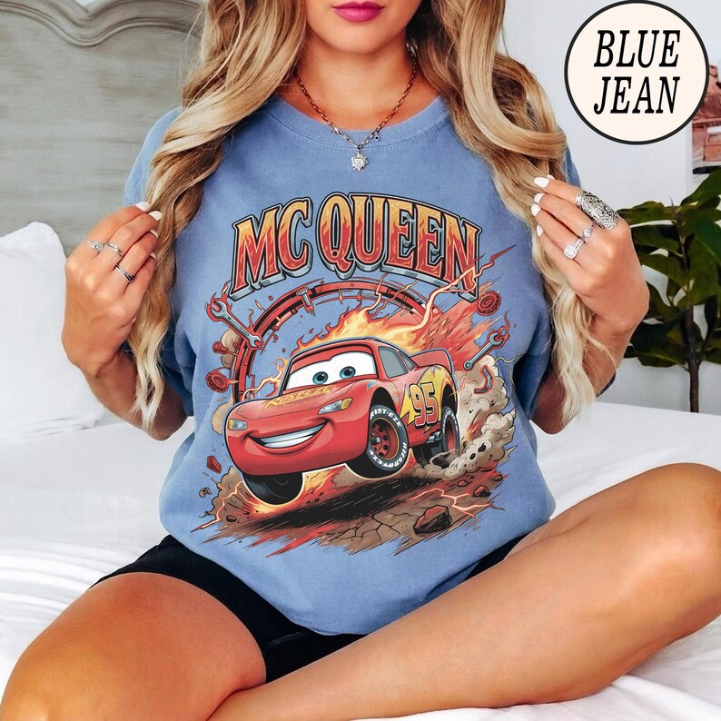 Puede incluir: Una camiseta azul con un gr&aacute;fico del coche de carreras rojo Lightning McQueen y el texto MC QUEEN encima. El dise&ntilde;o incluye llamas, herramientas mec&aacute;nicas y el n&uacute;mero 95 en el coche. La camiseta tiene un cuello redondo.