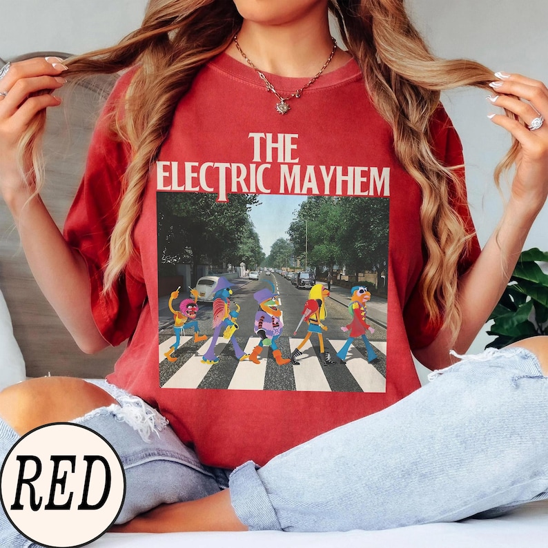 Pode incluir: T-shirt vermelho com gr&aacute;fico "The Electric Mayhem". O gr&aacute;fico mostra personagens dos Muppets parodiando a capa do &aacute;lbum Abbey Road dos Beatles, atravessando uma rua. A camiseta &eacute; de cor vermelha lisa.