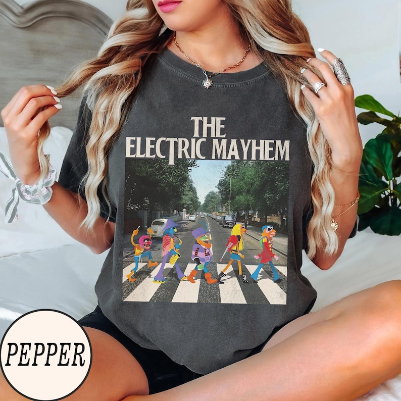 Pode incluir: Camiseta cinza escuro com "The Electric Mayhem" atravessando uma rua, uma par&oacute;dia da capa do &aacute;lbum Abbey Road dos Beatles. O gr&aacute;fico mostra personagens Muppet coloridos em uma faixa de pedestres. A camiseta tem um visual vintage.