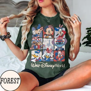 May include: Dark green t-shirt featuring a grid of Disney characters in patriotic attire. The shirt includes Mickey Mouse, Minnie Mouse, Donald Duck, and Goofy, with the text "Walt Disney World" below the grid.