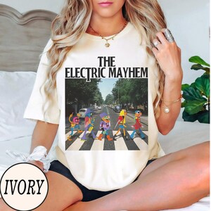 Pode incluir: Camiseta cor marfim com gr&aacute;fico "The Electric Mayhem". O gr&aacute;fico mostra personagens dos Muppets atravessando uma rua, semelhante &agrave; capa do &aacute;lbum Abbey Road dos Beatles. A camiseta &eacute; de estilo casual e unissex.
