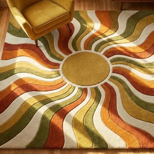 Pode incluir: Um tapete colorido com um design retro. O tapete apresenta um círculo amarelo central rodeado por ondas radiantes de laranja, verde, amarelo e branco. Uma poltrona amarela está sobre o tapete, que está sobre um chão de madeira.