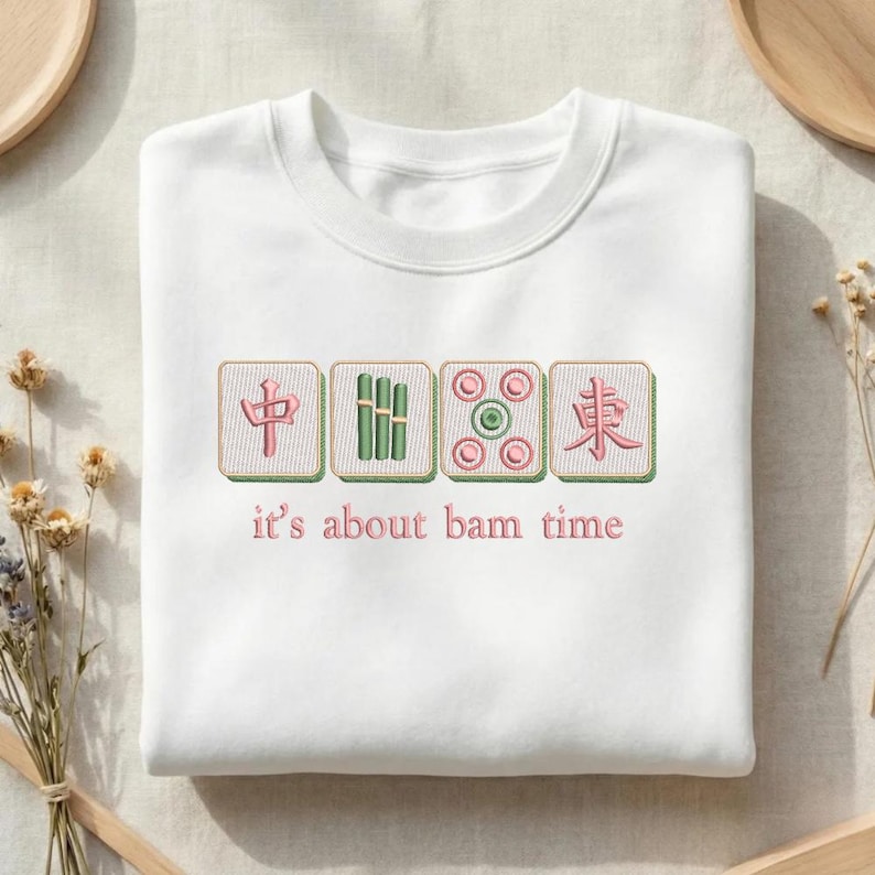 May include: White sweatshirt with embroidered Mahjong tiles in green and pink. The text "it's about bam time" is below the tiles. The sweatshirt is a crew neck style.