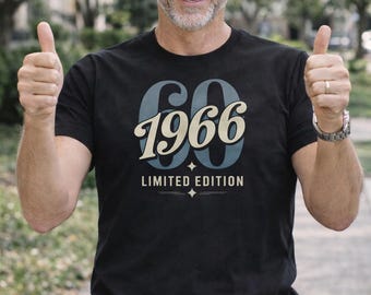 Peut inclure: T-shirt noir avec l'inscription "60 1966 ÉDITION LIMITÉE" dans un design rétro. Le t-shirt est porté avec un jean bleu et une ceinture marron. La personne fait un signe de pouce.