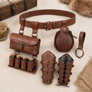 May include: A brown leather belt set featuring a rectangular pouch with four small corked glass vials, a drawstring pouch with an embossed circular design, two buckled arm guards, and a leather key ring with a brass-toned metal ring.