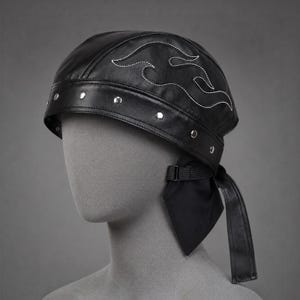 May include: A black leather skull cap featuring white flame embroidery on the crown, a wide band accented with silver-toned metal studs, and a black fabric tie closure at the back with an adjustable plastic buckle for a secure fit.
